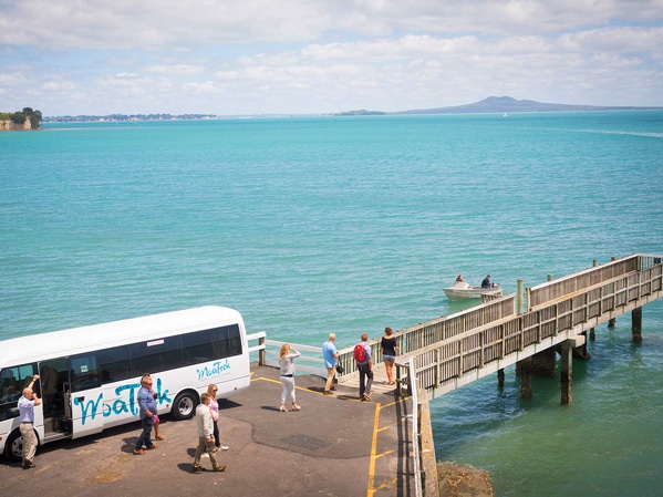 Moatrek bus parked by a wharf overlooking Rangitoto