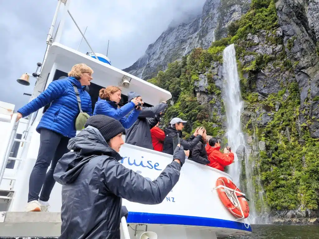 Travellers taking photos of the waterfalls on a Milford Sound small boat cruise, New Zealand