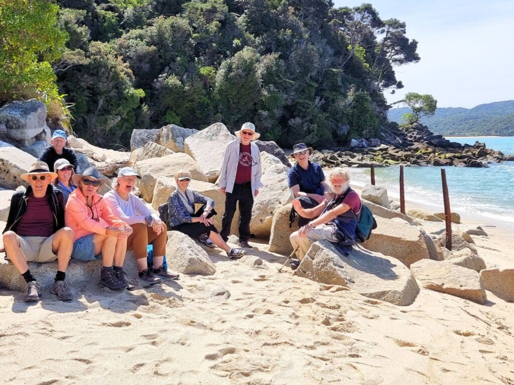 A group of over-50 travellers on resting on the beach in the Abel Tasman National Park, New Zealand