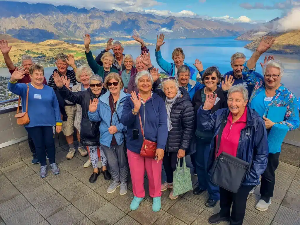 A group of over-50 travellers waving to the camera at the Queenstown Gondola lookout
